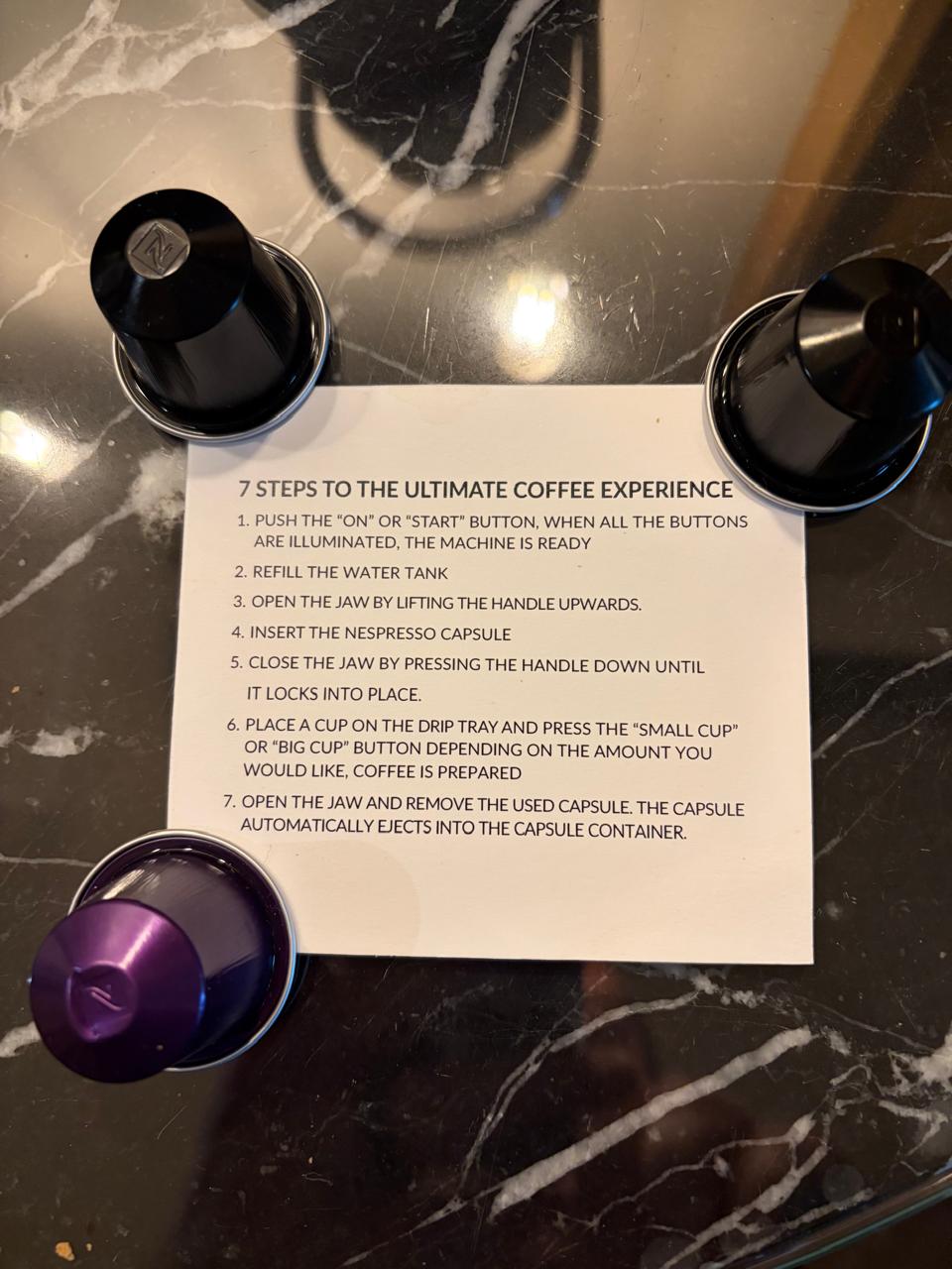 Hotel instruction card titled 7 Steps to the Ultimate Coffee Experience surrounded by Nespresso capsules on a marble counter