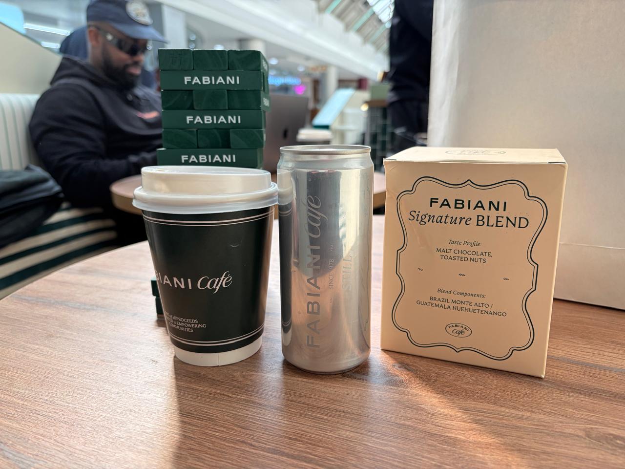 The Fabiani Signature Blend box alongside a Fabiani Café takeaway cup and a Fabiani-branded still water can, with green Fabiani Jenga blocks in the background