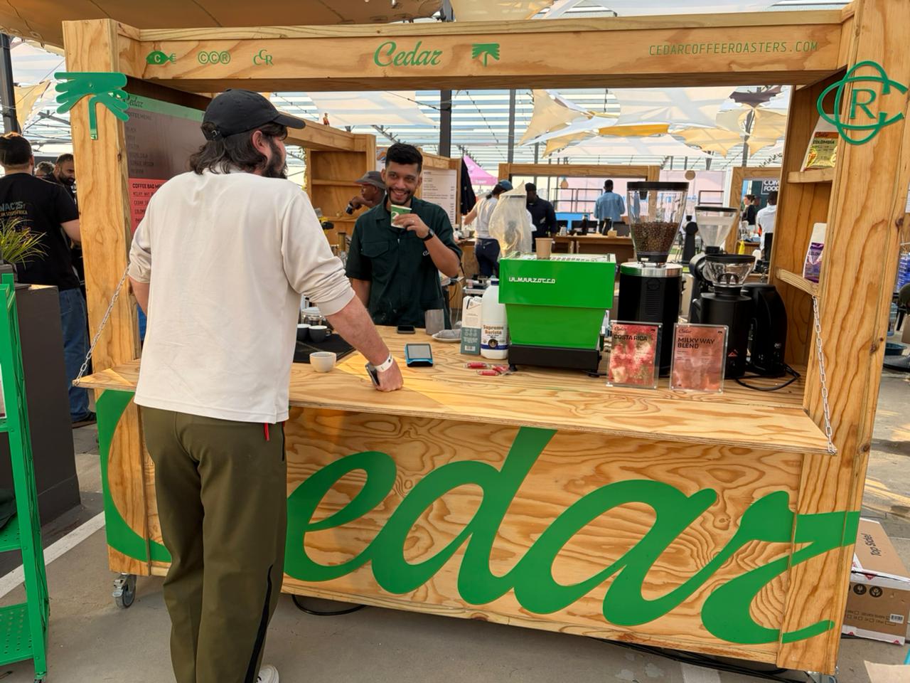Cedar Coffee Roasters stand at Jo'burg Coffee Festival 2026 — green branding, Milky Way and Costa Rica bags, green La Marzocco