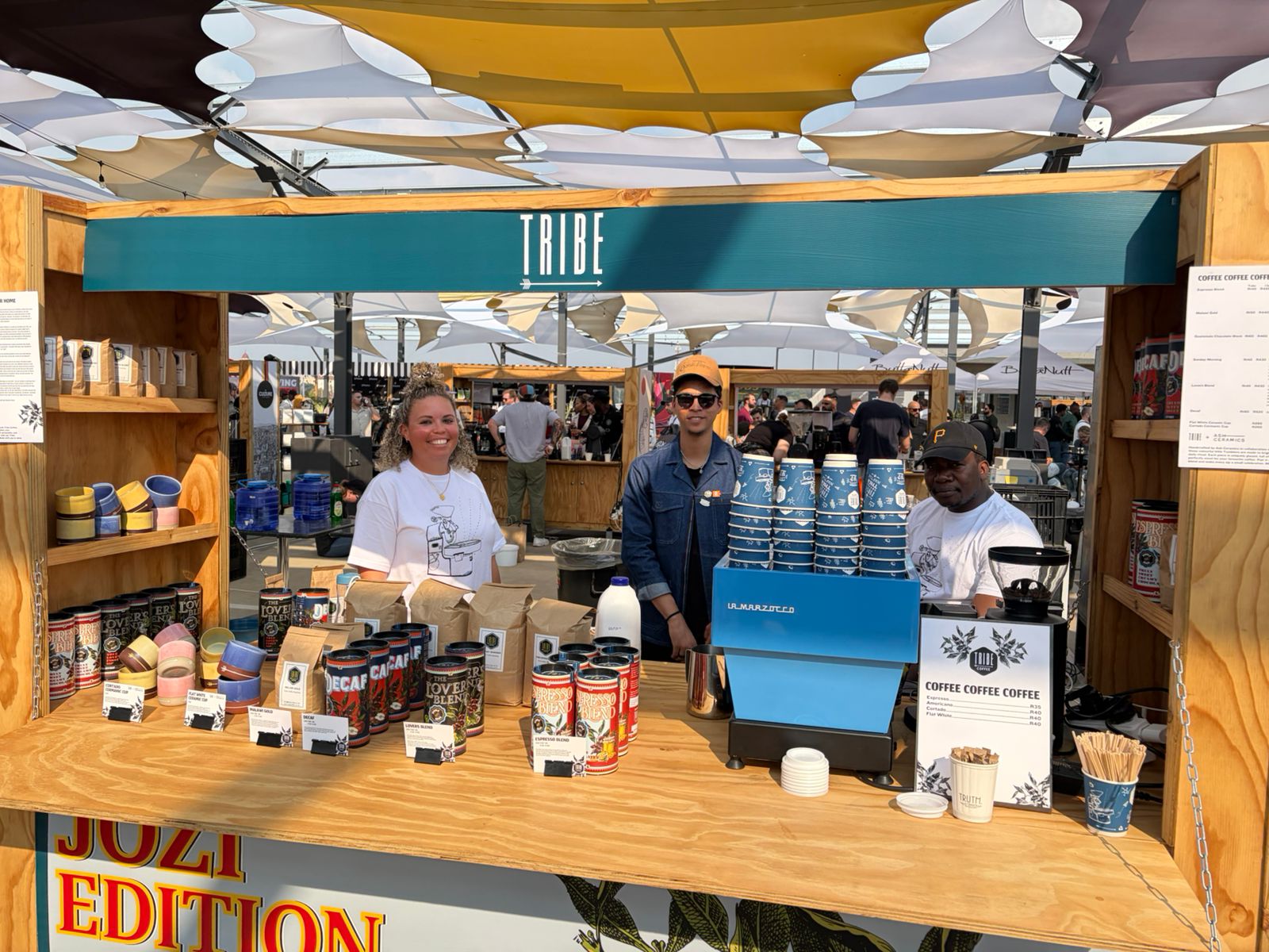 Tribe Coffee stand at Jo'burg Coffee Festival 2026 — three team members, La Marzocco, JOZI EDITION signage