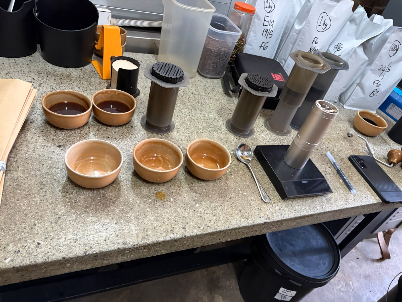 Handmade ceramic cupping bowls alongside AeroPress brewers and a precision scale on the QC counter