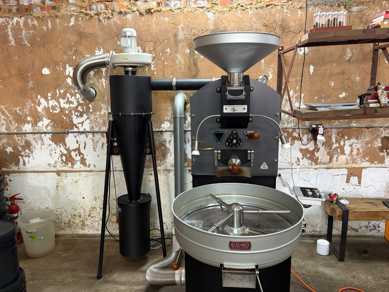 The Genio coffee roaster at Sorcery — matte black drum roaster with cherry-wood knobs, cooling tray, and cyclone chaff collector