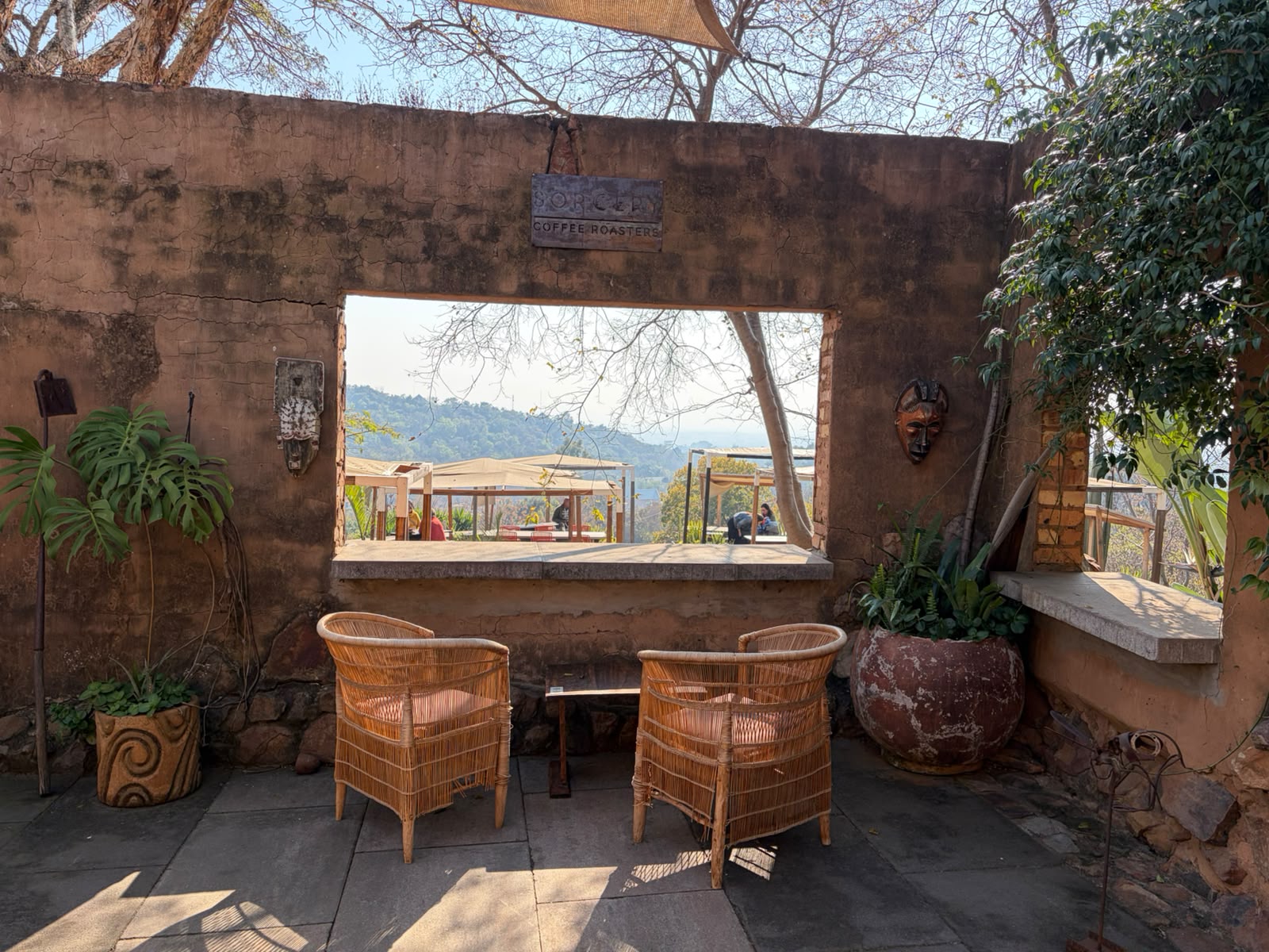 Two wicker chairs framing a stone window looking out to the outdoor deck and valley, Sorcery Coffee Roasters sign above