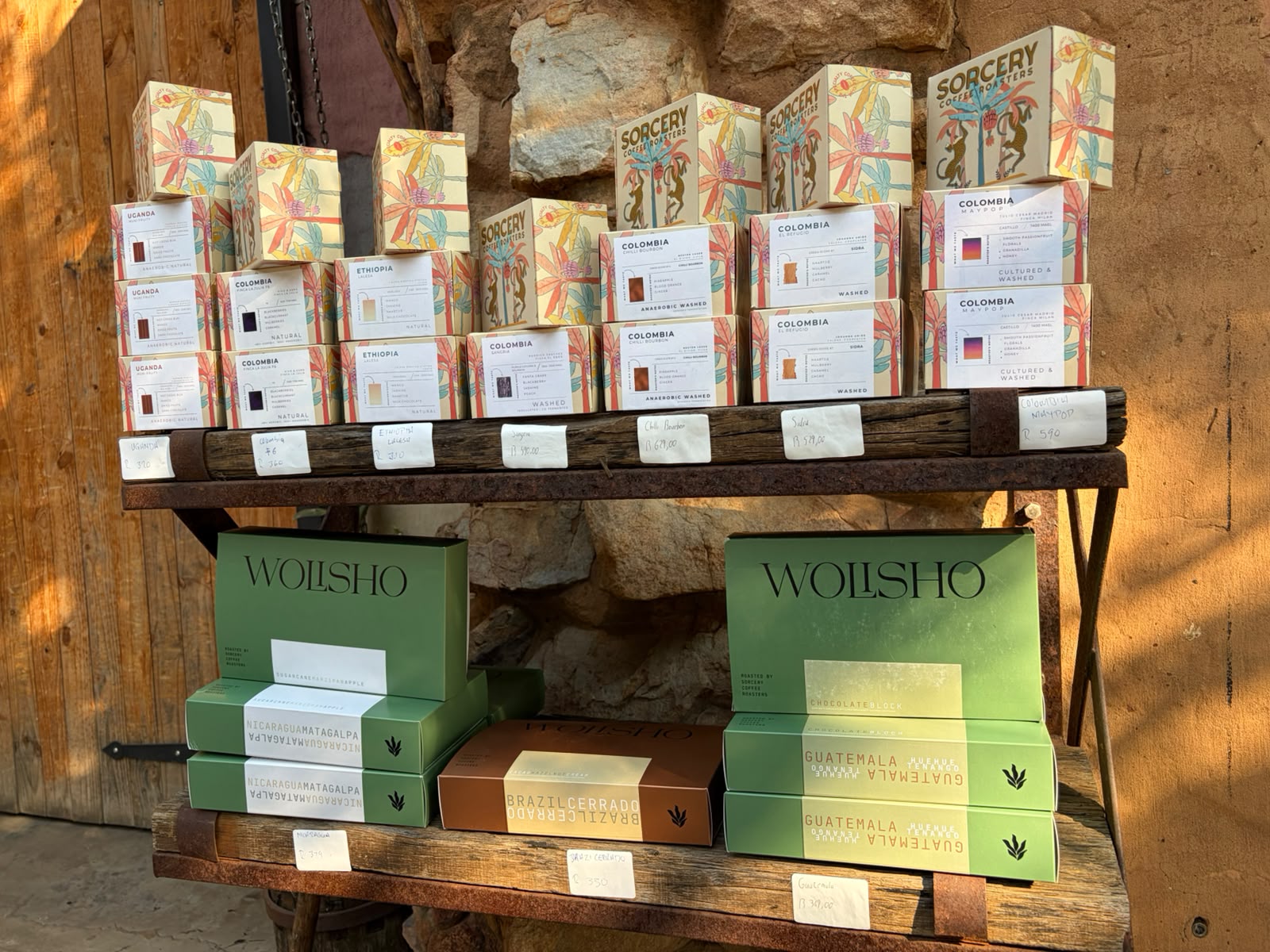 Sorcery Coffee boxes (tropical motif packaging) and Wolisho boxes (olive green) displayed on a rustic timber shelf