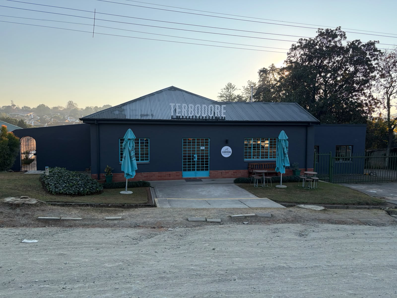 Terbodore Coffee Roasters building exterior — dark grey walls, teal umbrellas, blue doors, corrugated iron roof