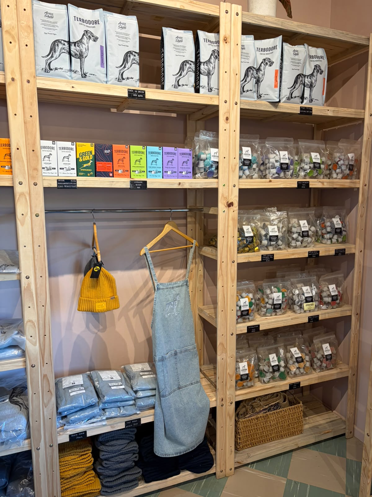 Merch shelf — Terbodore hoodies on hangers, folded t-shirts, yellow beanie, denim apron, Nespresso capsule bags