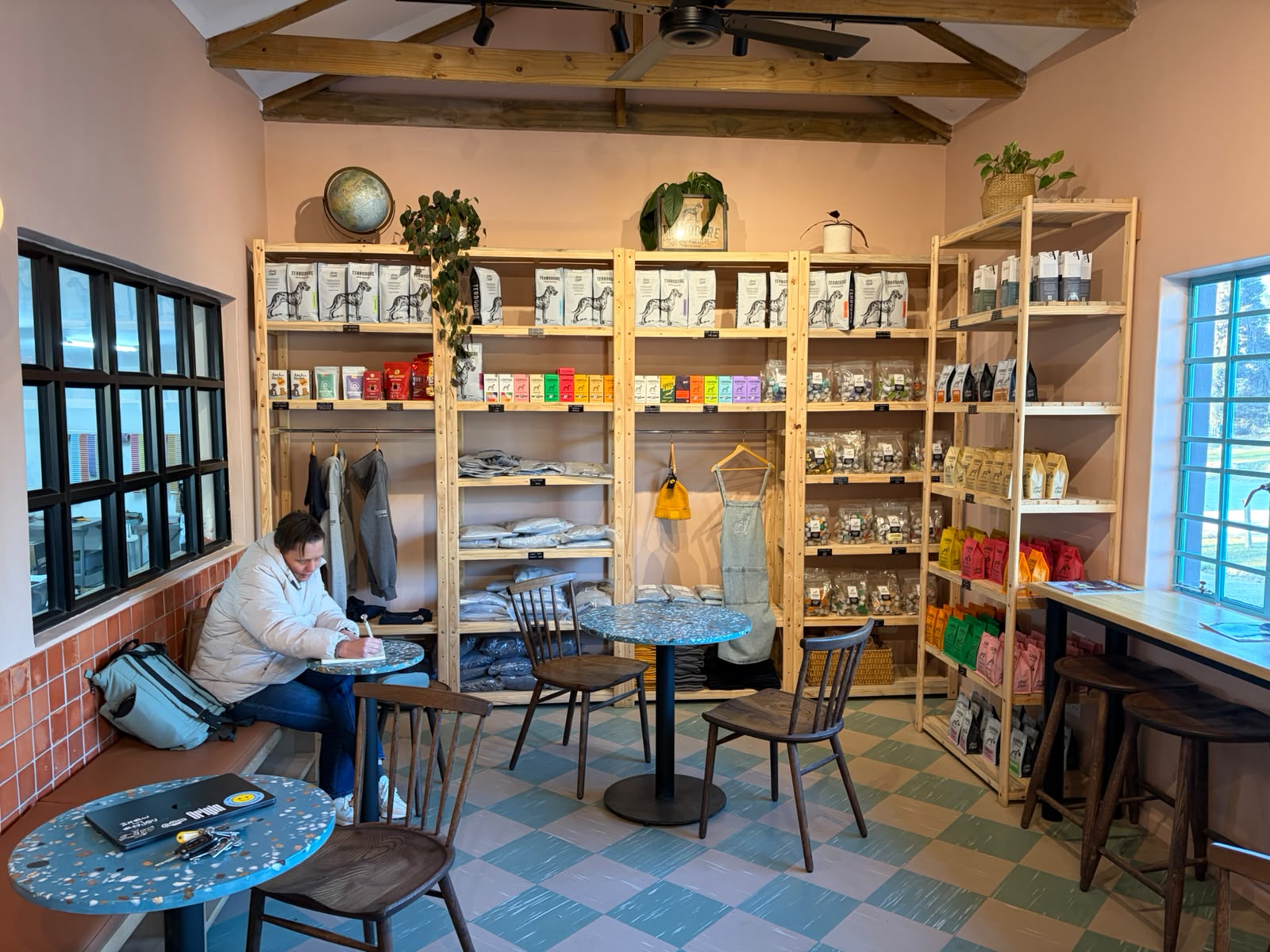 Wide shot of the retail area — wooden shelves floor to ceiling, Terbodore bags in every colour, a customer writing at a terrazzo table