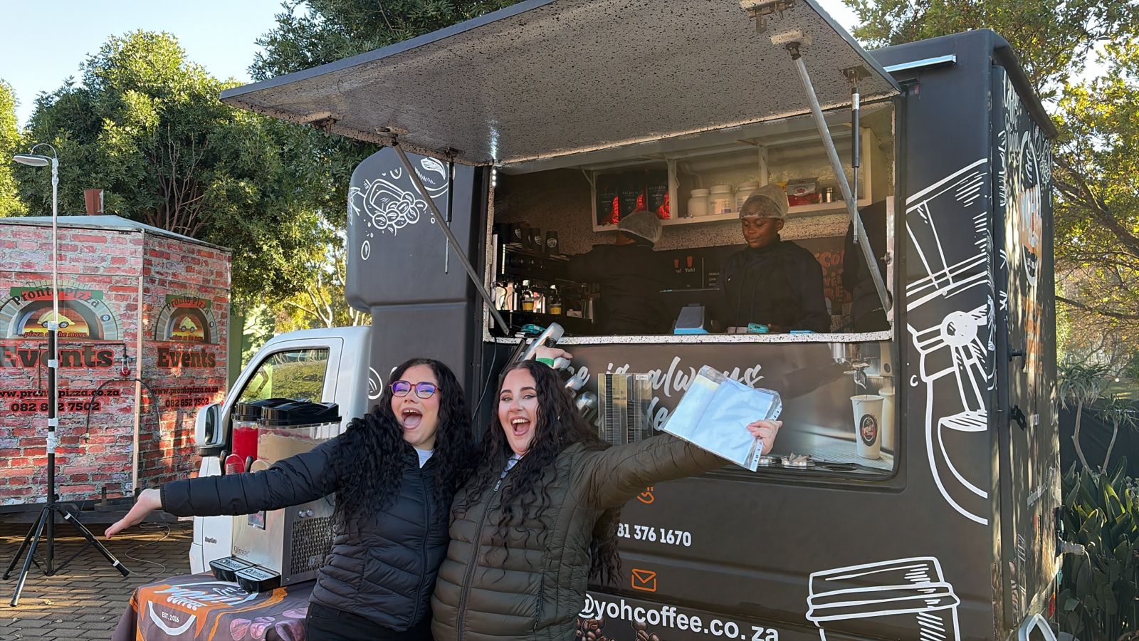 Two happy customers posing in front of the Yoh Coffee truck at Ellis Park