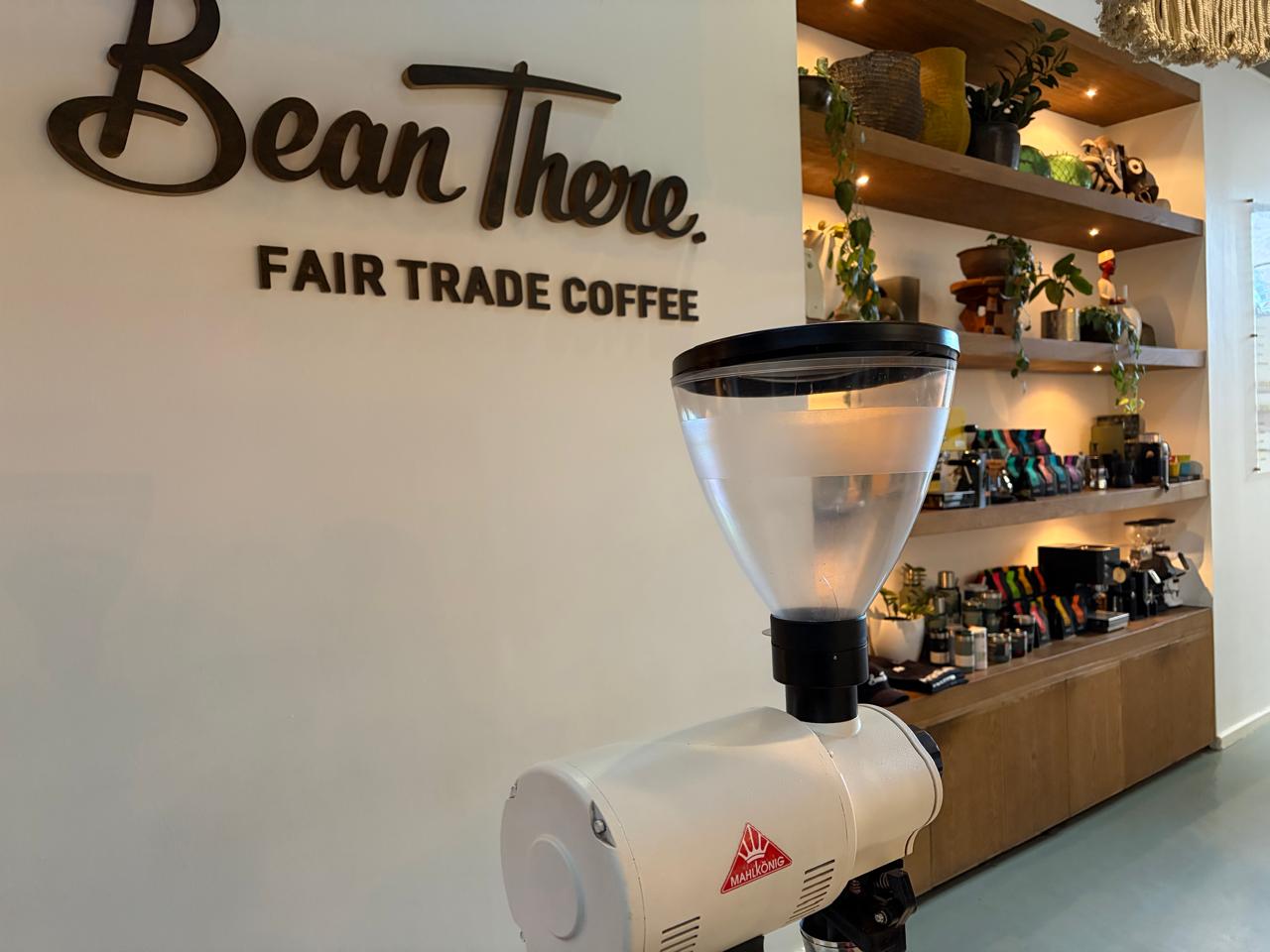 Close-up of the Bean There wall signage and white Mahlkönig grinder at 44 Stanley — retail bags in rainbow colours on the shelves behind
